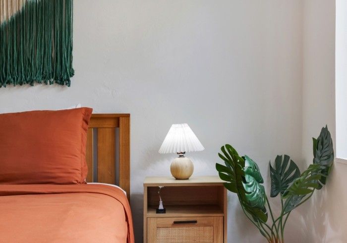 Orange bed beside wooden nightstand with lit lamp and green plants in a minimalist bedroom