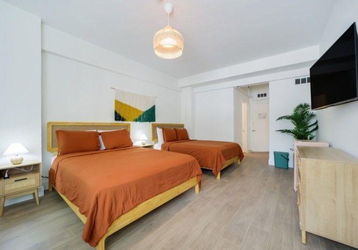 Bright bedroom with two orange beds, white walls, wood floor, and a wall-mounted TV