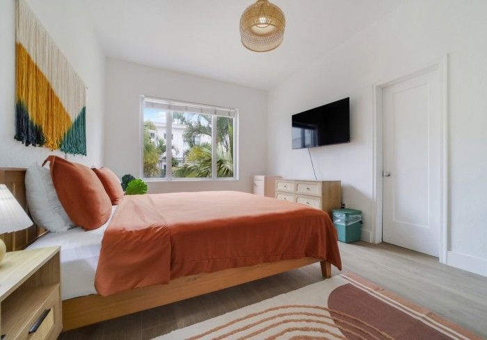Bright bedroom with coral bedding, wall-mounted TV, window, and striped rug