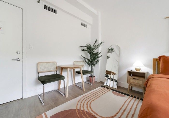 Bright minimalist living room with orange sofa, chair, plant, mirror, and small table near a white wall