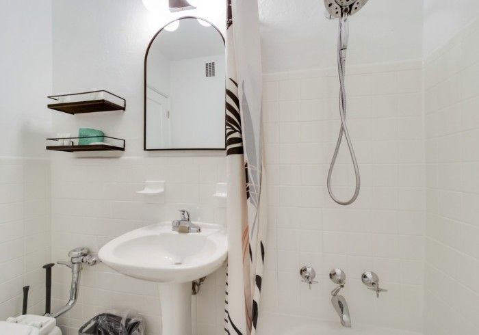 Small white bathroom with sink, mirror, shelves, and a shower with striped curtain.