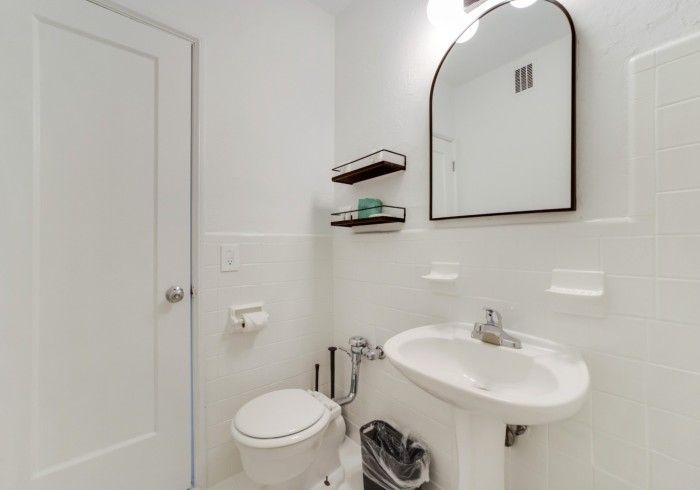 Small white bathroom with toilet, sink, mirror, and towel shelves