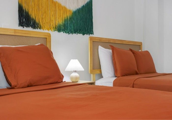 Two orange beds with white pillows and a small lamp in a bright bedroom