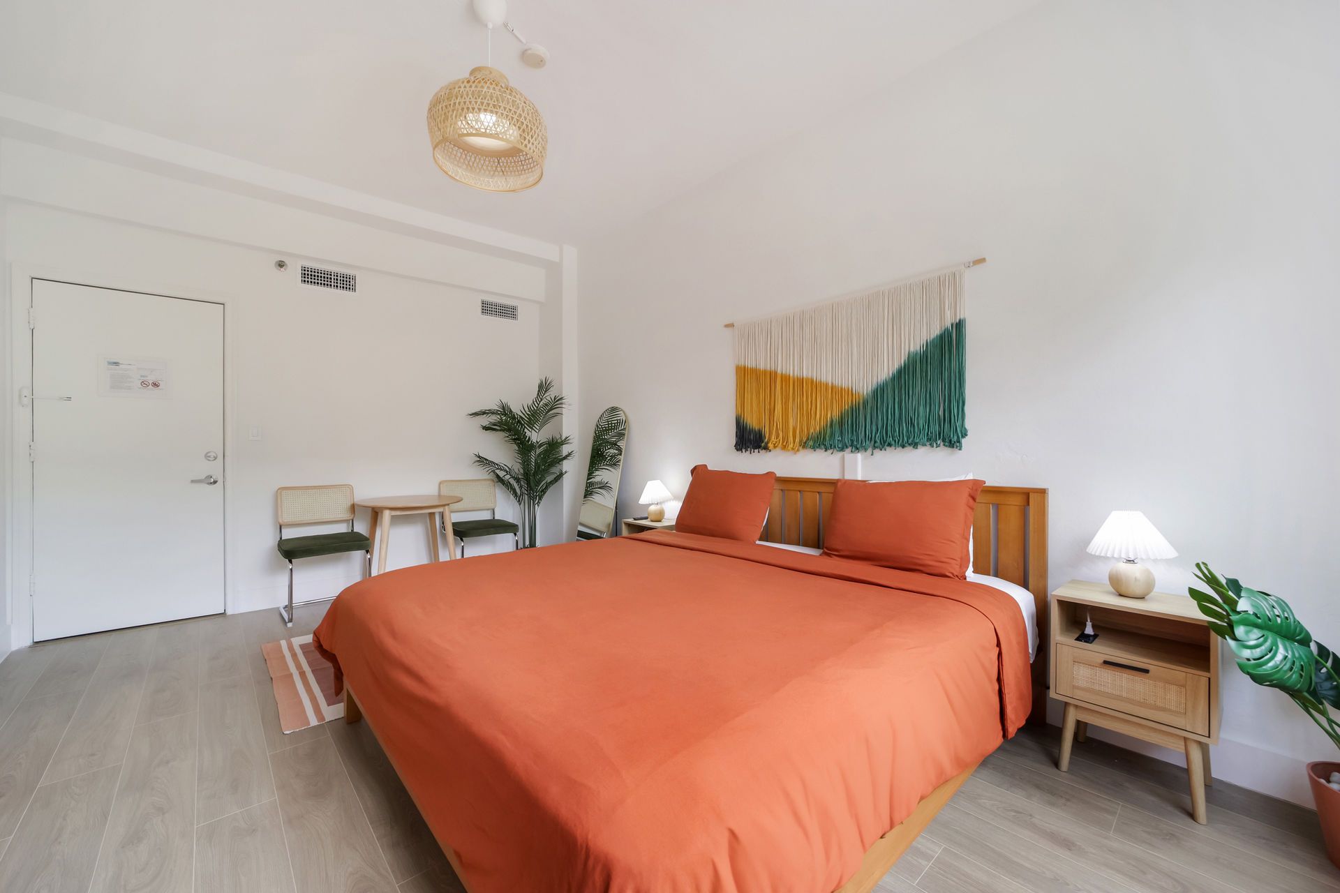 Bright bedroom with orange bedspread, wooden nightstands, desk, and wall art in a minimalist white room