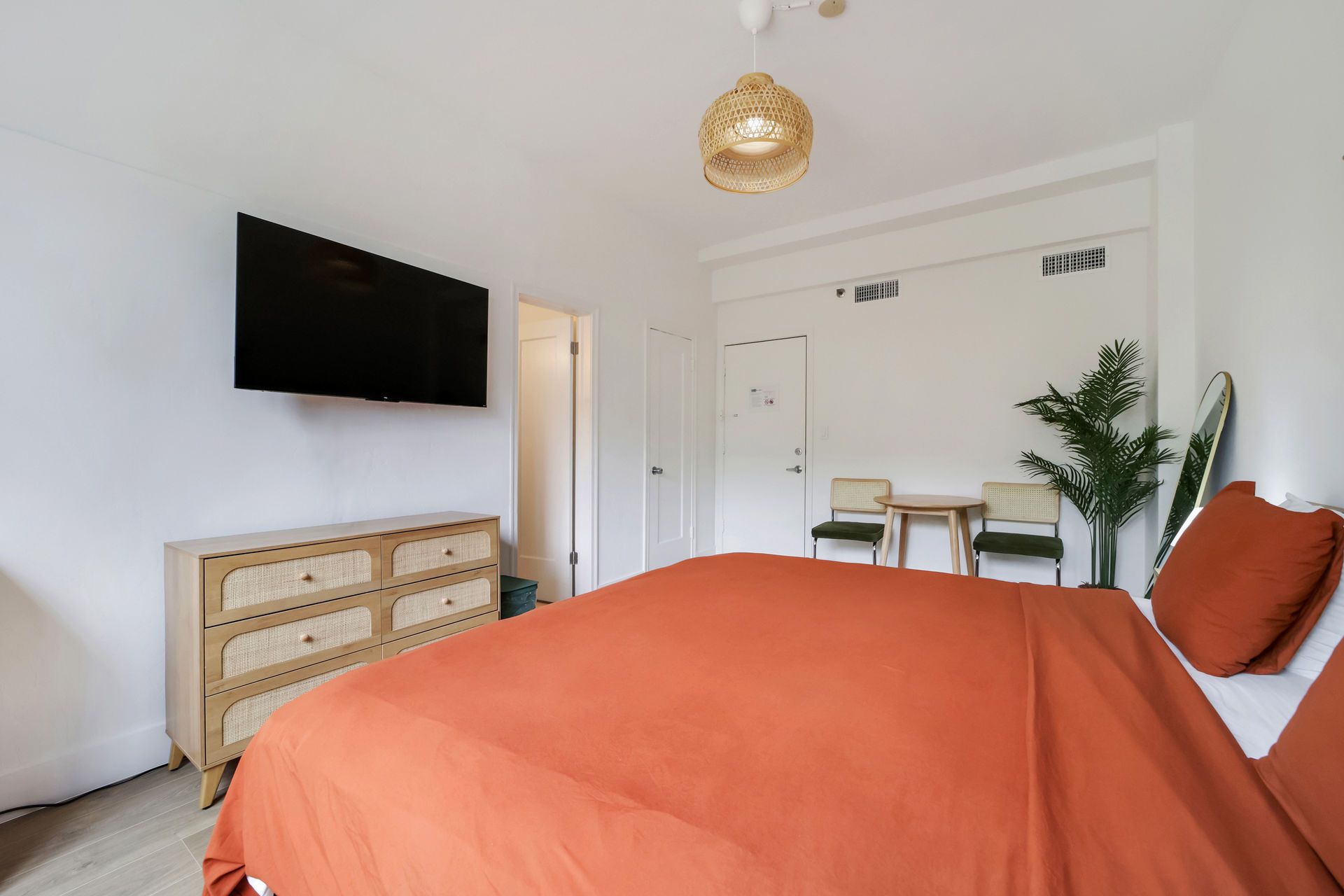 Modern bedroom with orange bedspread, wall-mounted TV, dresser, and desk by the window