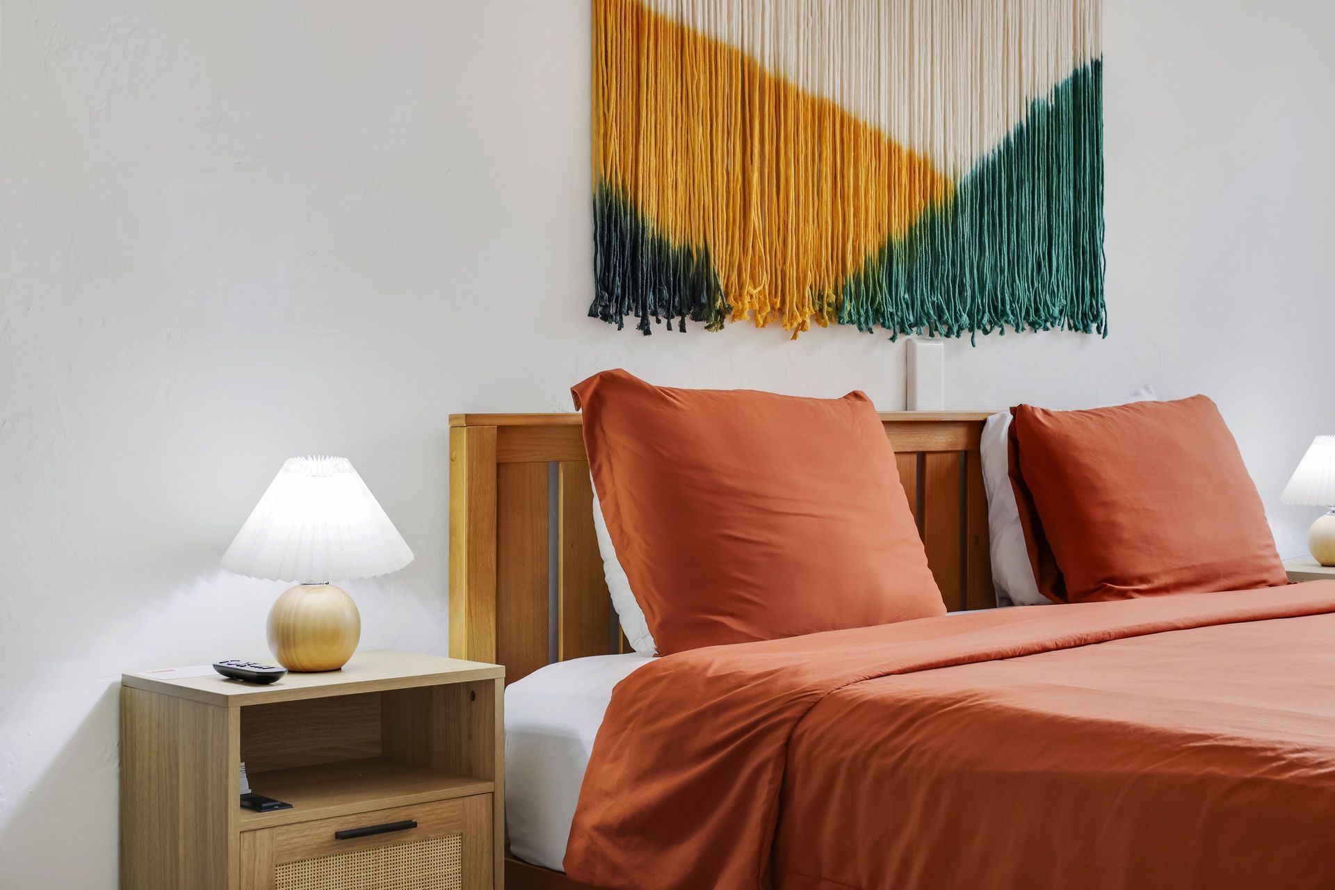 Cozy bedroom with terracotta bedding, wooden nightstand, white lamp, and abstract wall art
