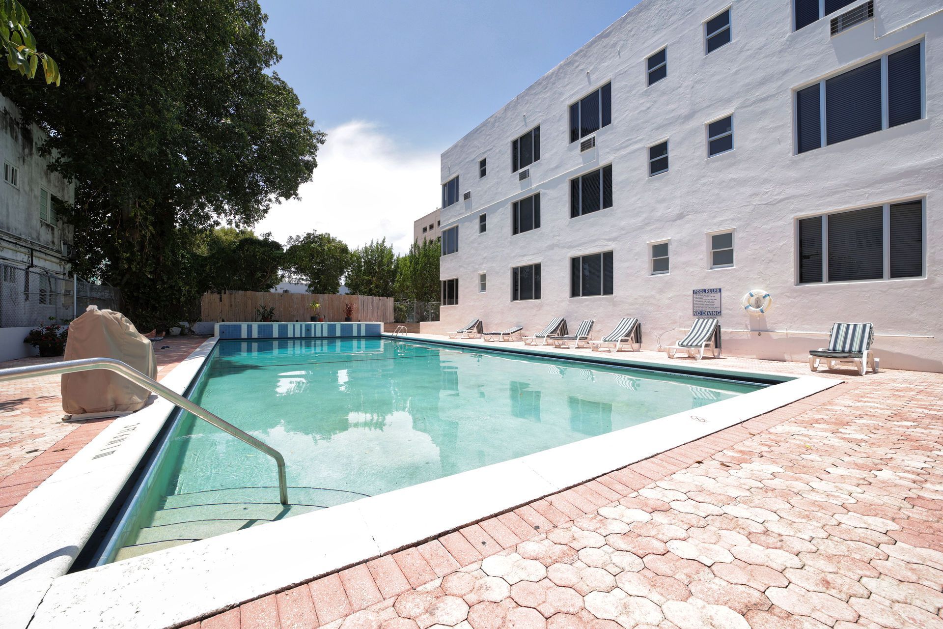 Outdoor hotel pool beside a white multi-story building with lounge chairs and stone deck