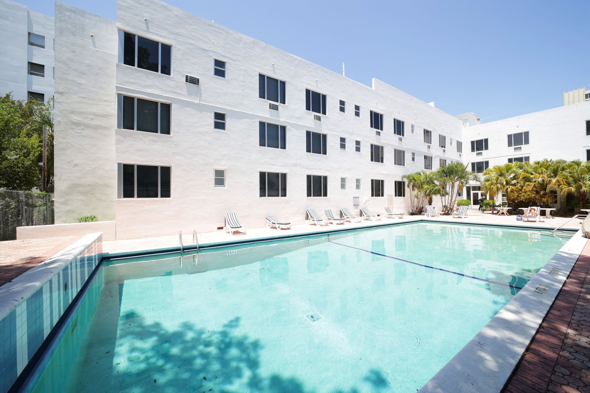 Outdoor swimming pool beside a white apartment building under a clear blue sky