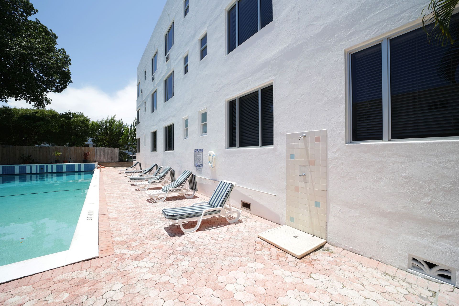 Poolside patio beside a white building with lounge chairs and blue-striped windows in bright sun