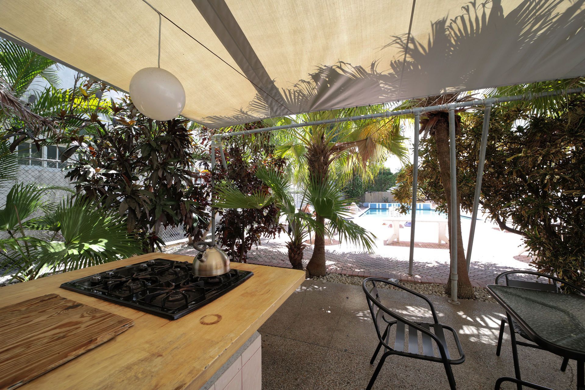 Shaded patio seating beside a pool with potted plants and a countertop under a canopy