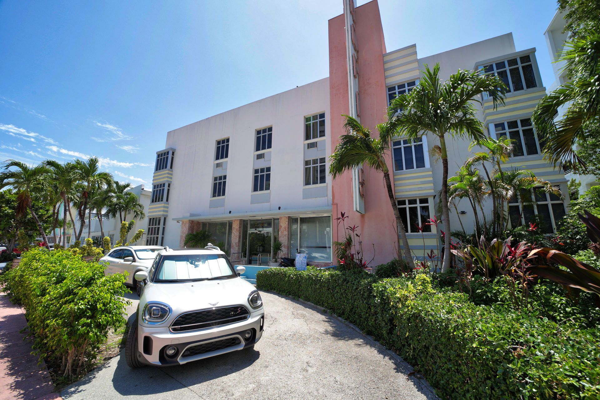 White SUV parked outside a modern white building with palm trees and hedges under a bright blue sky
