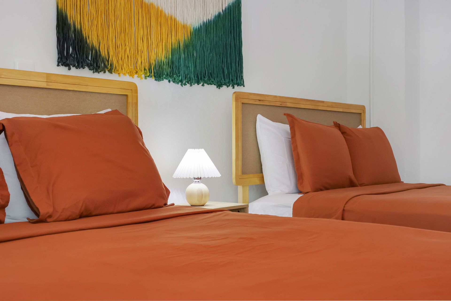 Two orange-covered twin beds with white pillows and a bedside lamp in a bright room