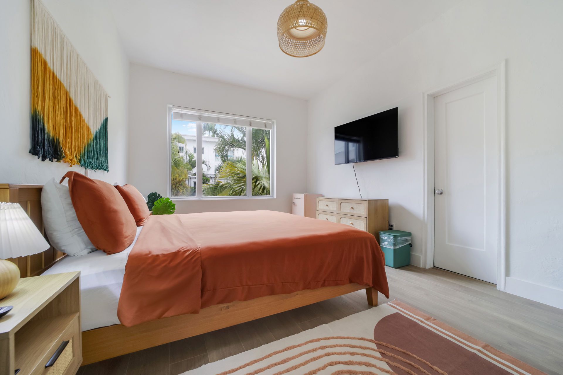 Bright bedroom with peach bedspread, wall art, TV, window, and white closet doors