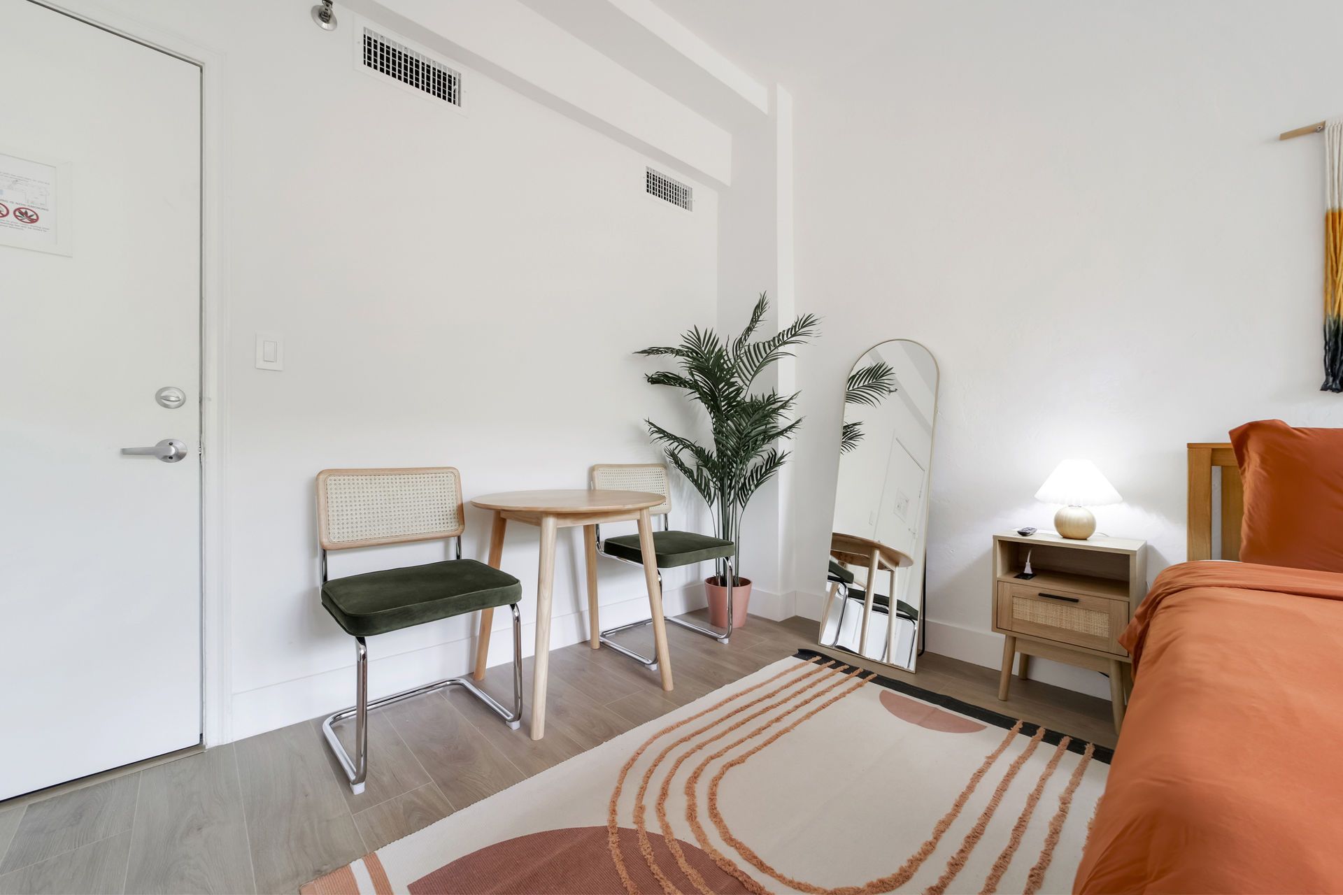 Bright minimalist bedroom with chair, desk, floor lamp, plant, mirror, and orange sofa