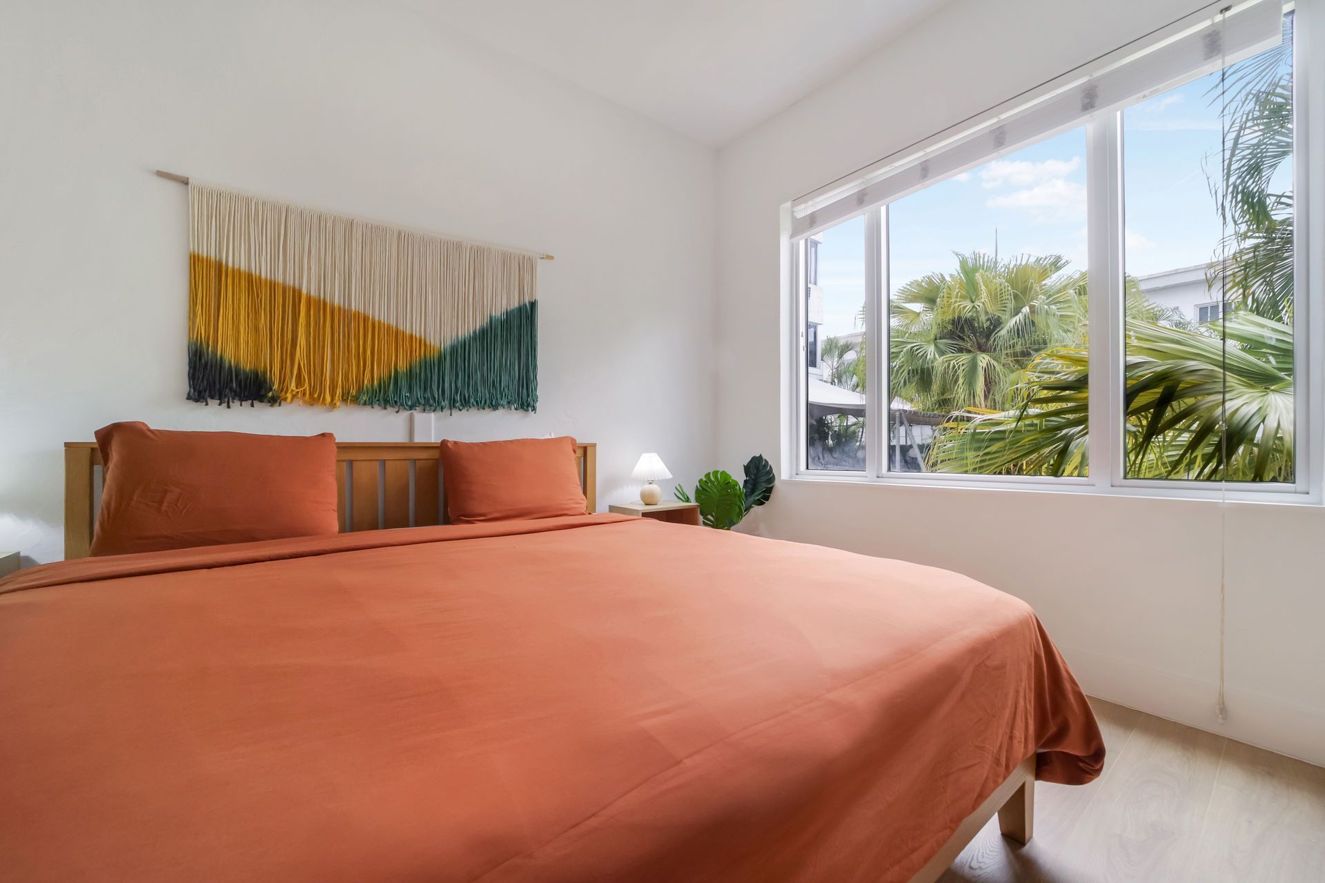 Bright bedroom with terracotta bedspread, wall art, and large window overlooking greenery