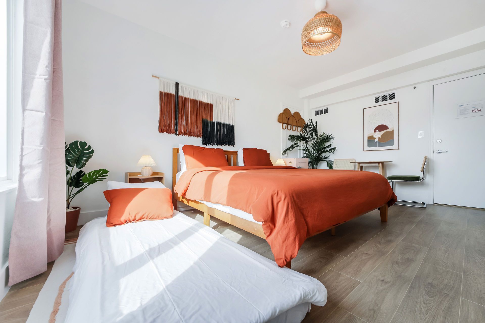 Bright bedroom with orange bedspread, white chair, plants, and sunlight on the floor