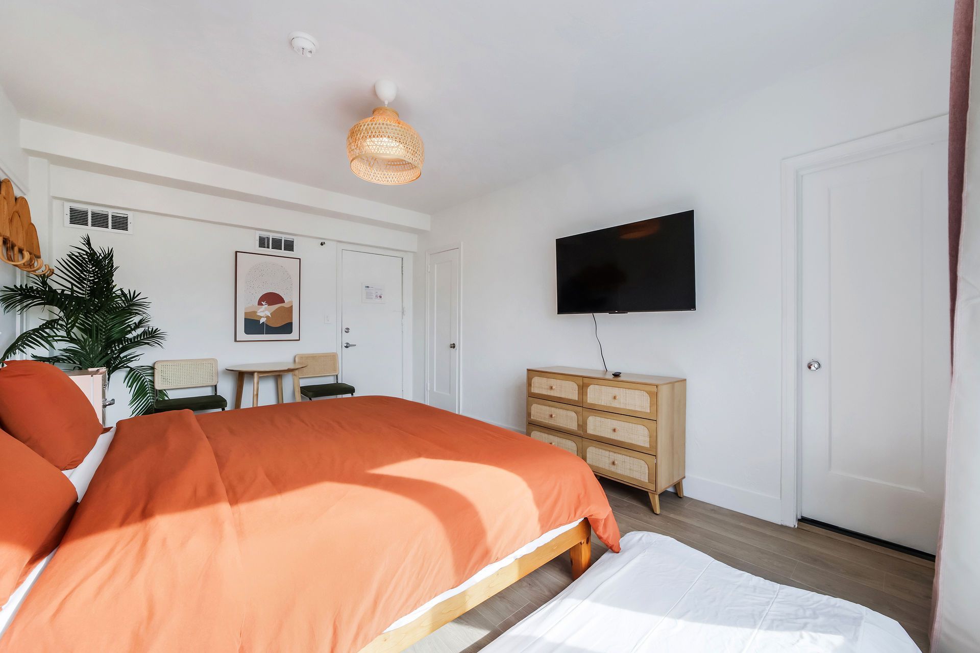 Bright bedroom with orange bedspread, wall-mounted TV, dresser, and white closet doors