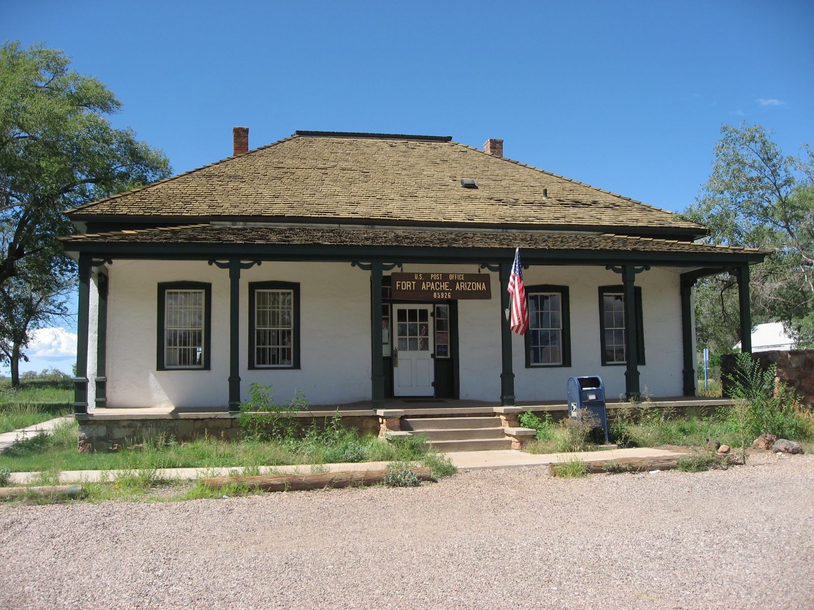 Historic stone building with porch and American flag under a clear blue sky
