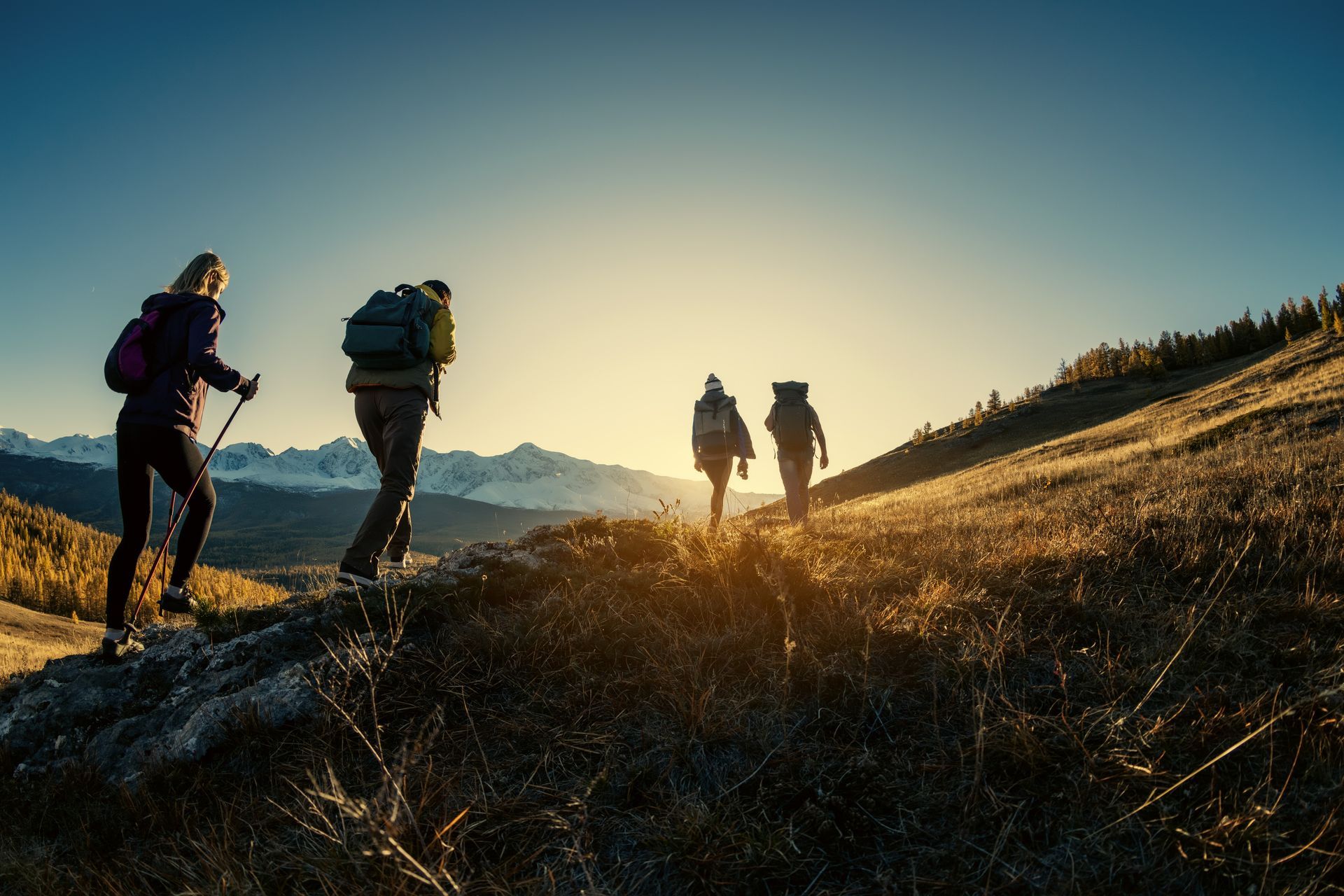 Four hikers silhouetted on a sunlit mountain trail at sunset