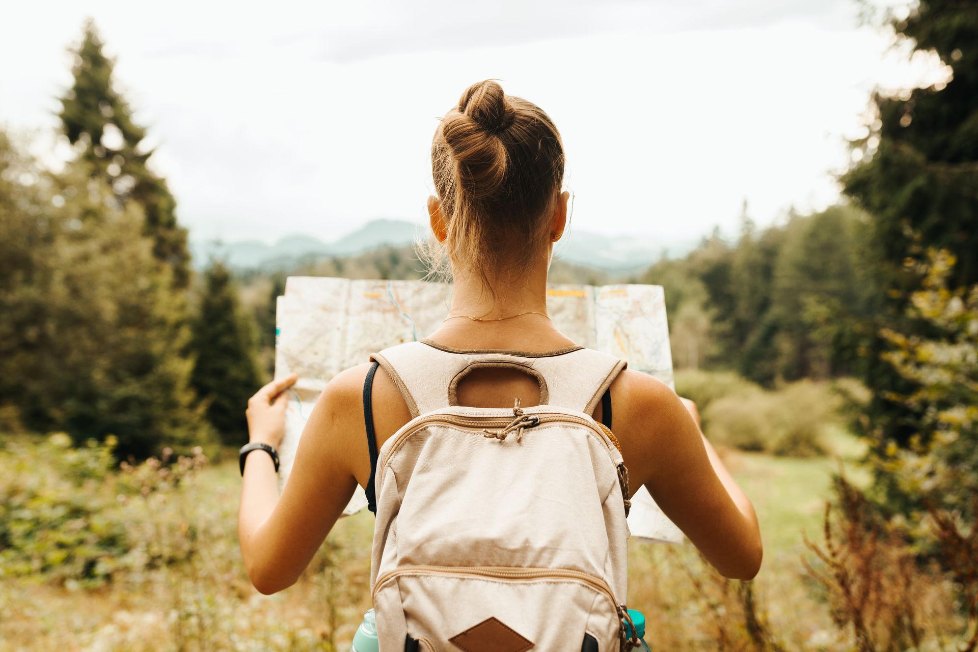Hiker with backpack reading a map on a forest trail, surrounded by trees and greenery