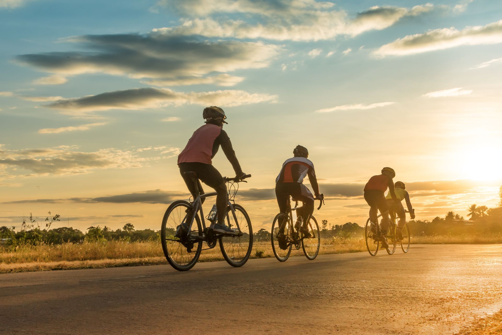 Cyclists riding on a road at sunset, with warm sky and open fields in the background