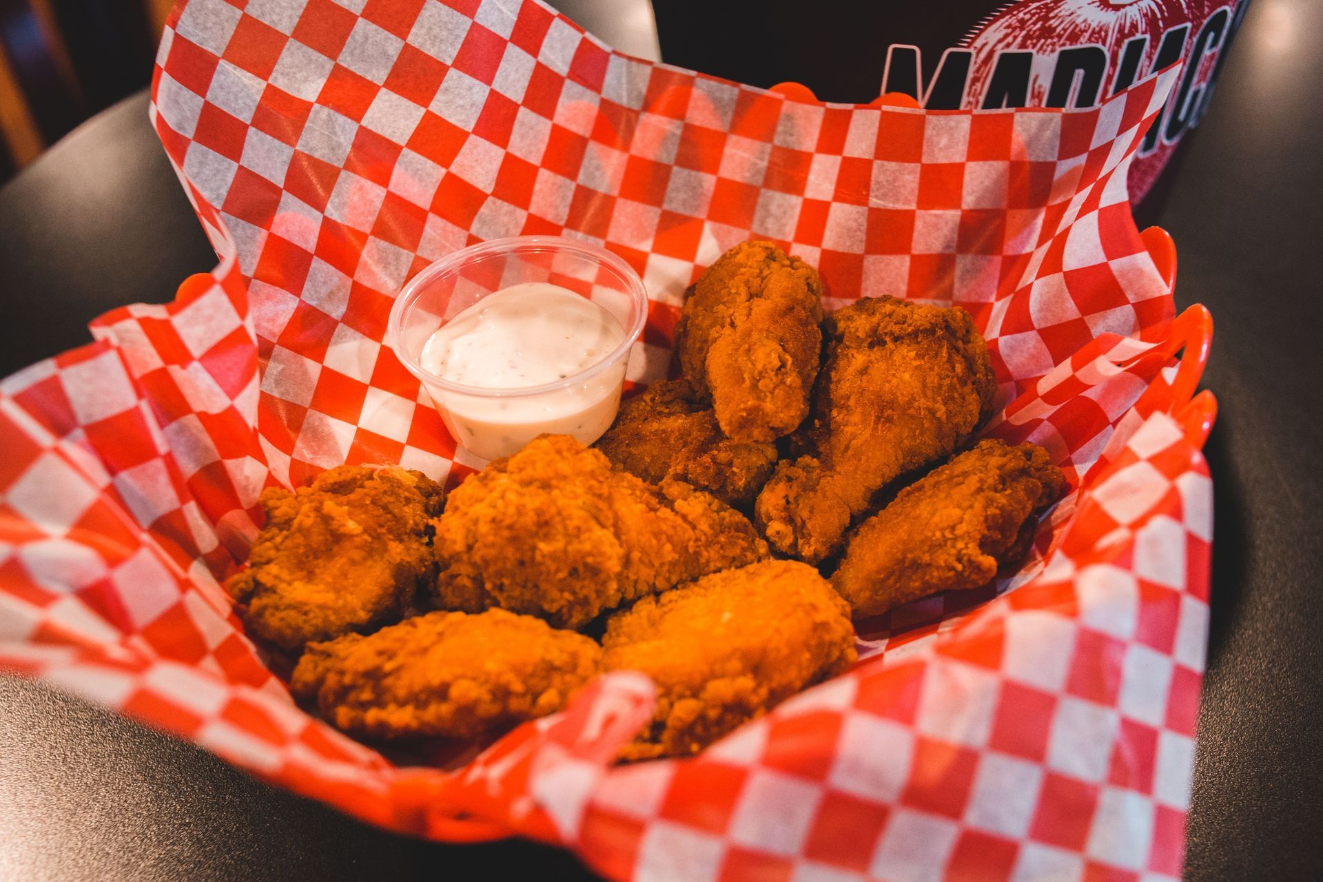 Basket of fried chicken nuggets with dipping sauce in red checkered paper