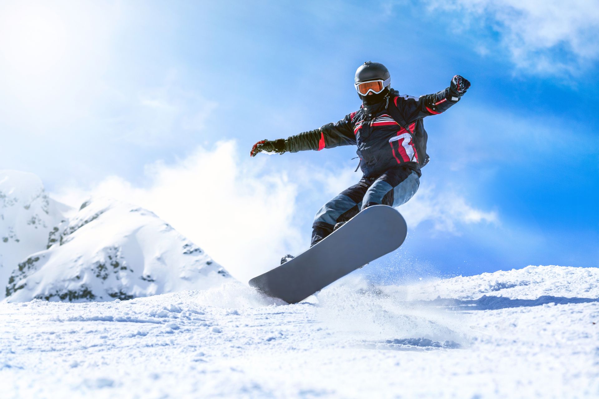 Snowboarder mid-jump over snowy terrain with mountains in the background