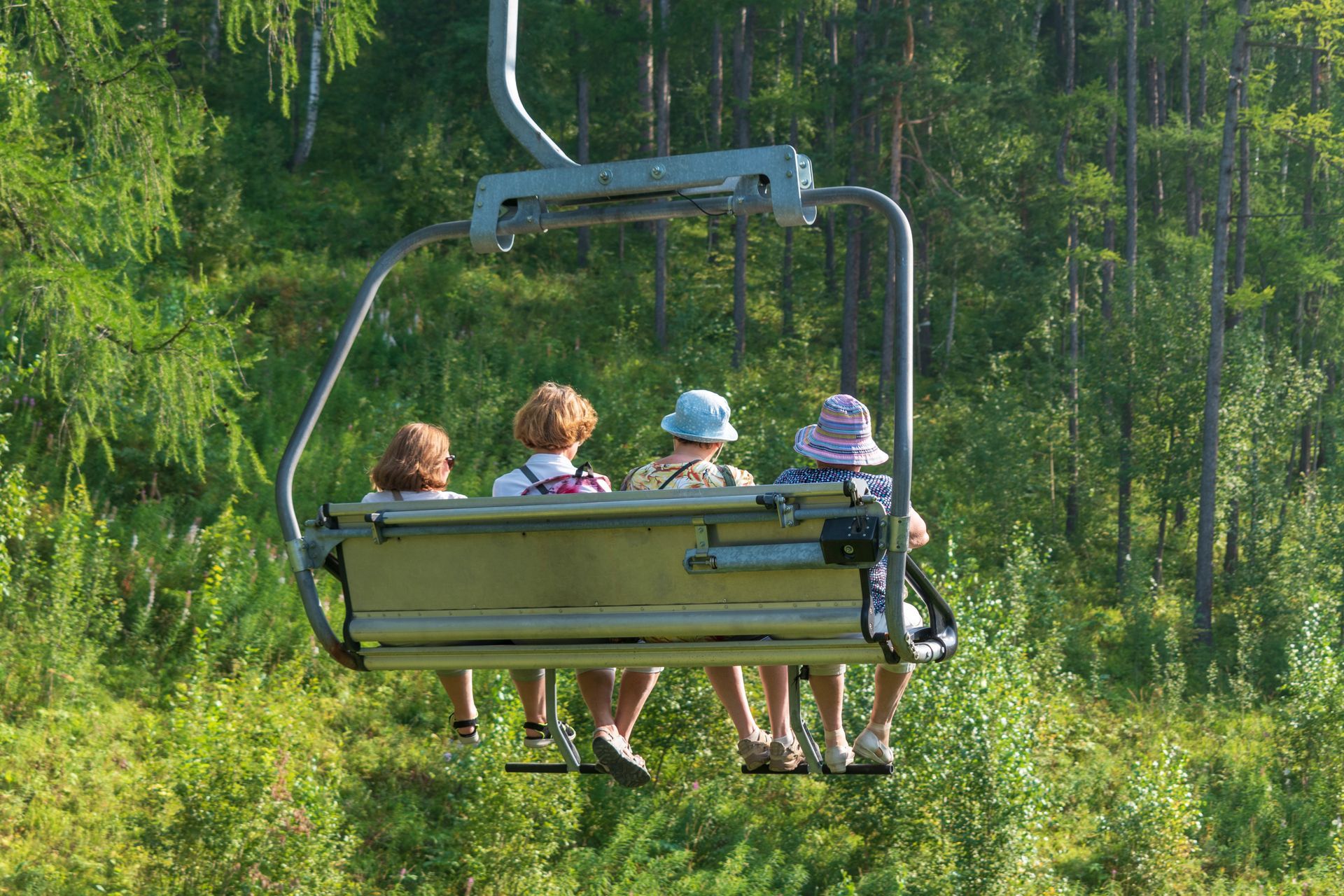 Four people riding a chairlift over a green forest