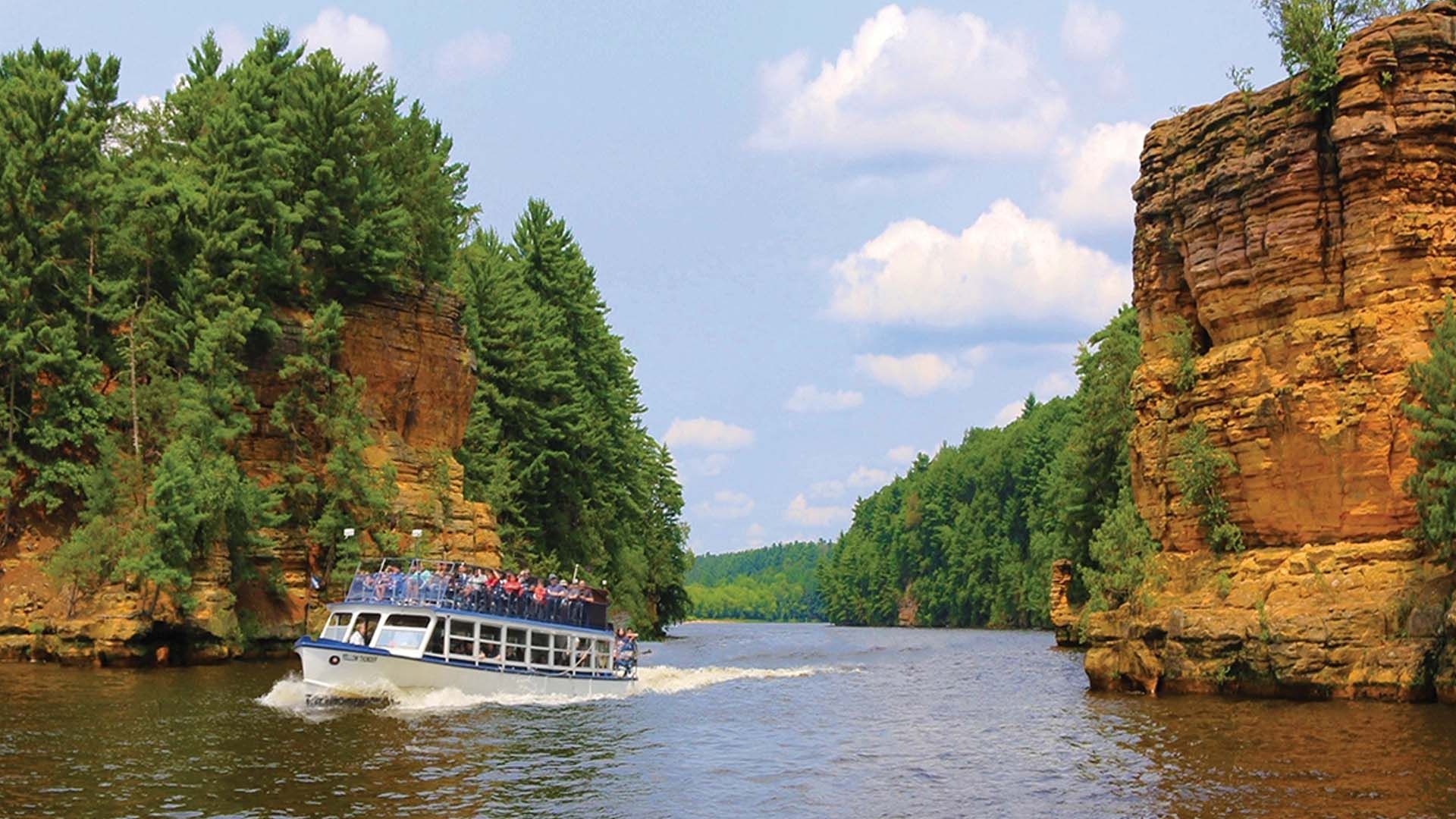 Sightseeing boat cruising along the Wisconsin River, passing through scenic sandstone cliffs in Wisconsin Dells.