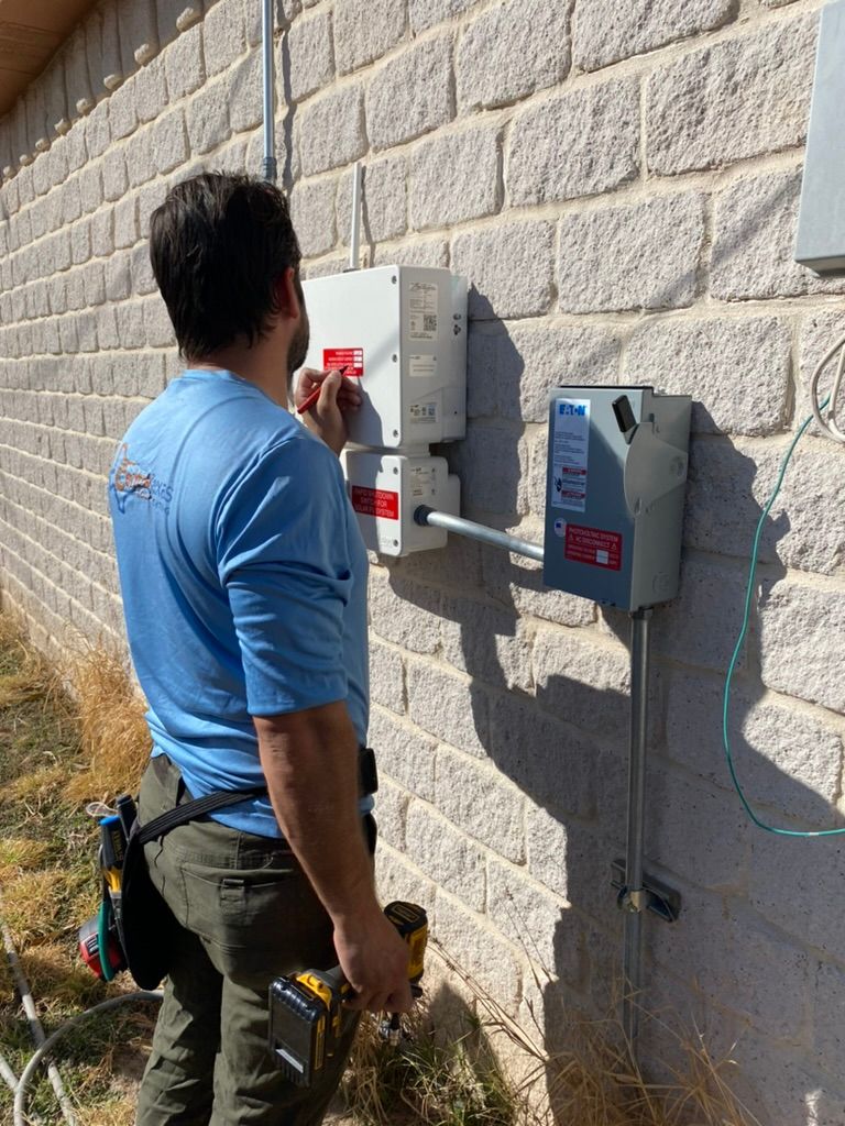 Technician in blue shirt inspecting an electrical panel on a brick wall outdoors.