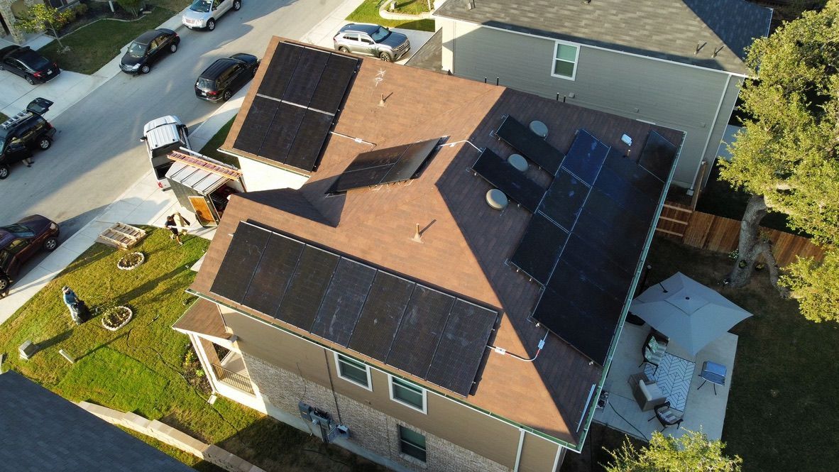 Aerial view of a tan house with a red roof and solar panels, beside a street with parked cars.