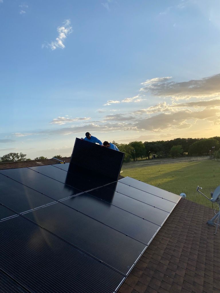 Solar panels on a rooftop at sunset, with a black vent or unit near the ridge.