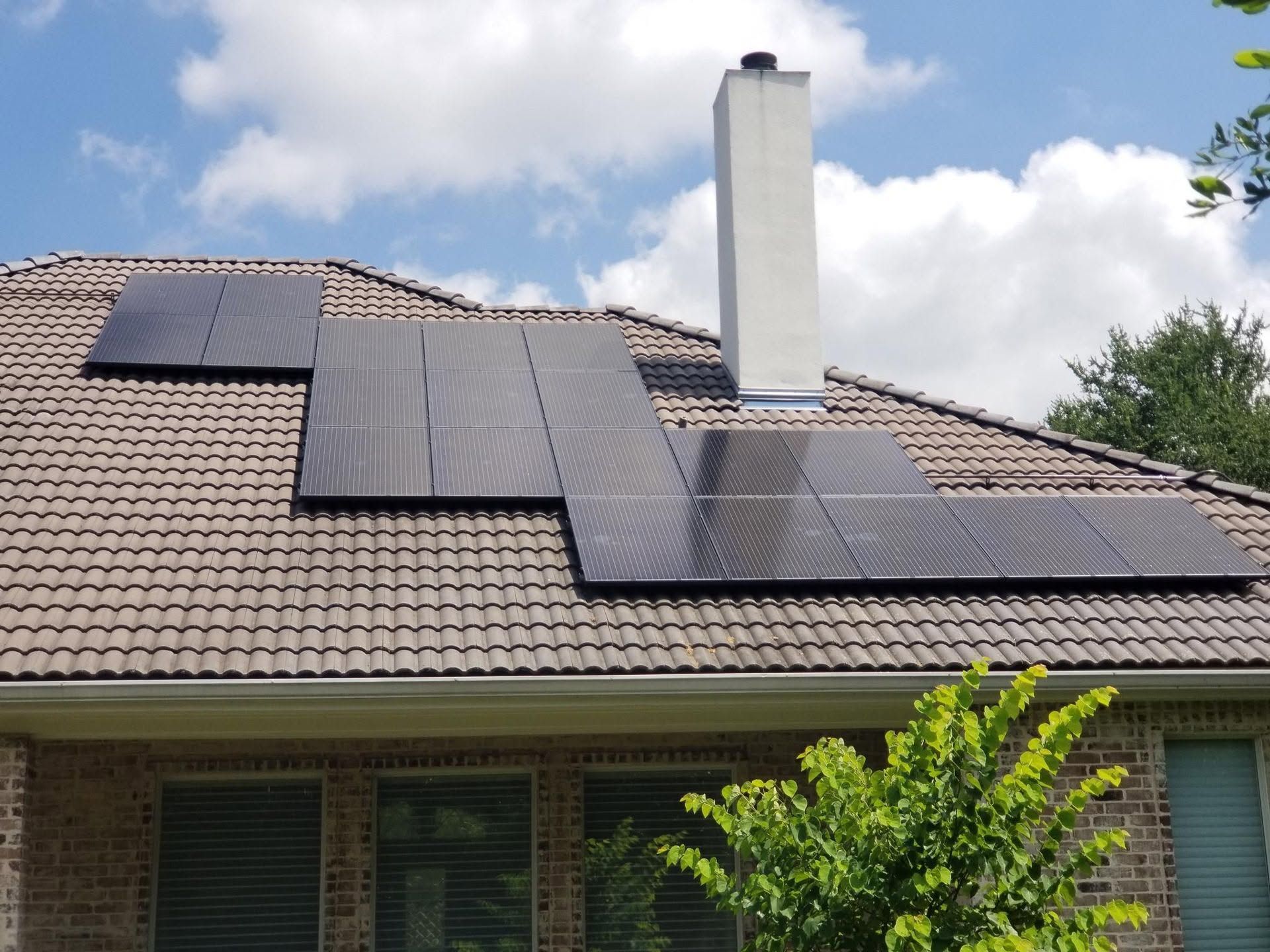 House roof with solar panels and a central chimney under a partly cloudy sky