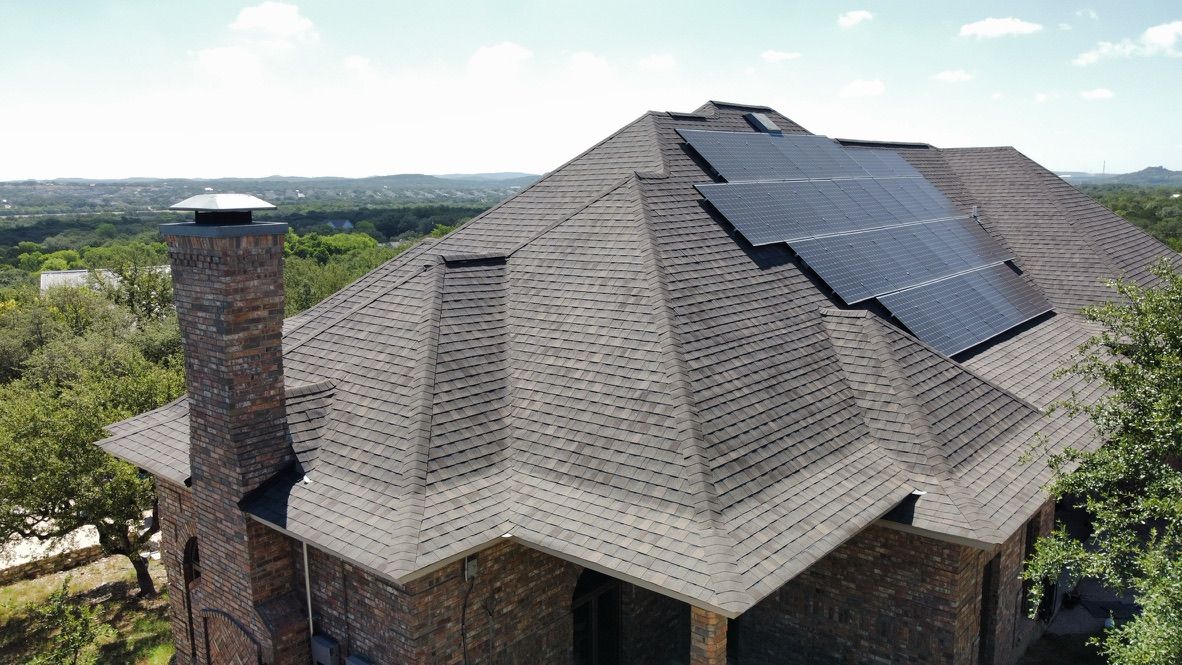 Aerial view of a house roof with solar panels and a chimney against a wooded landscape