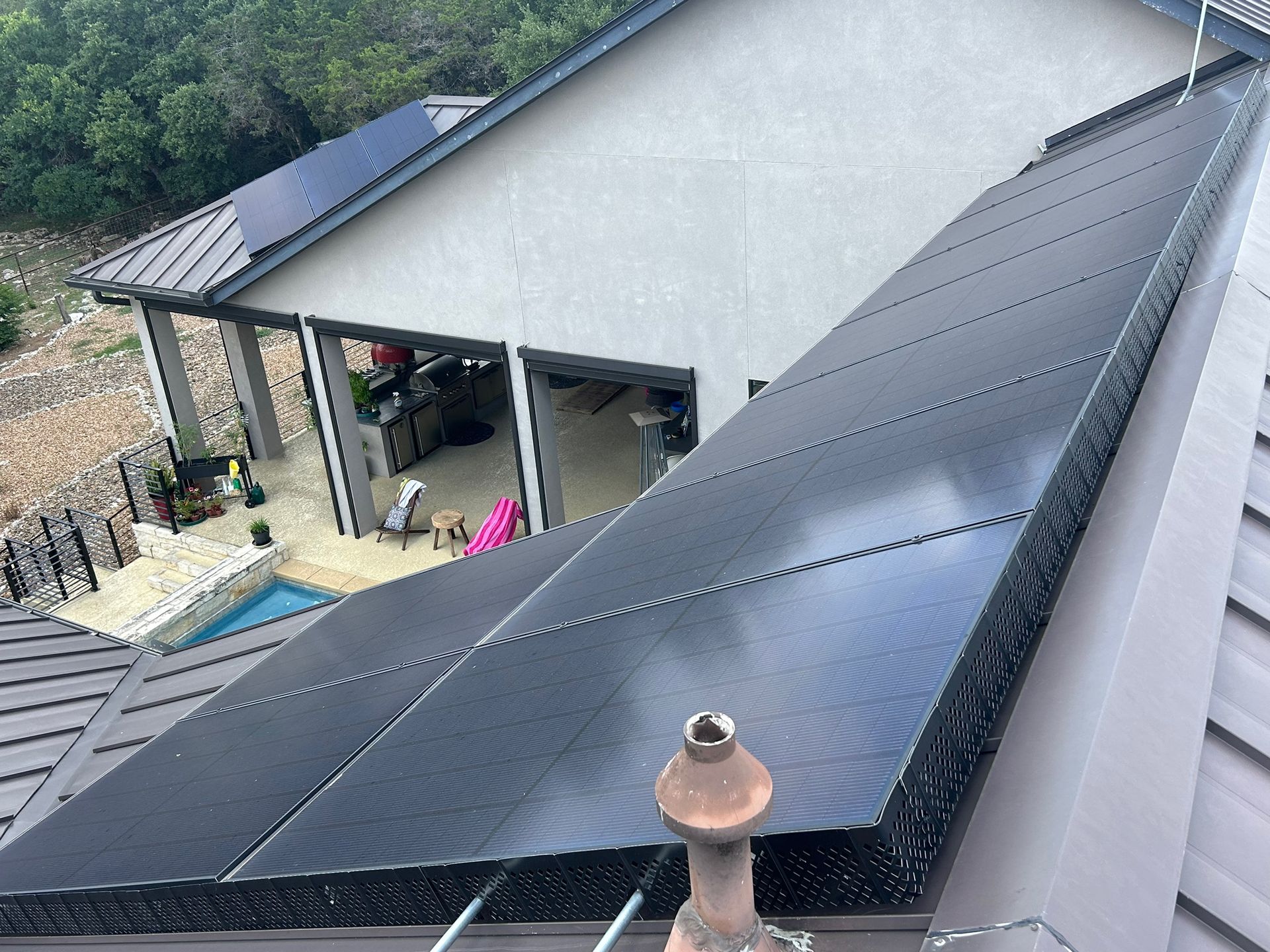 Solar panels on a gray house roof beside a covered patio and hillside.