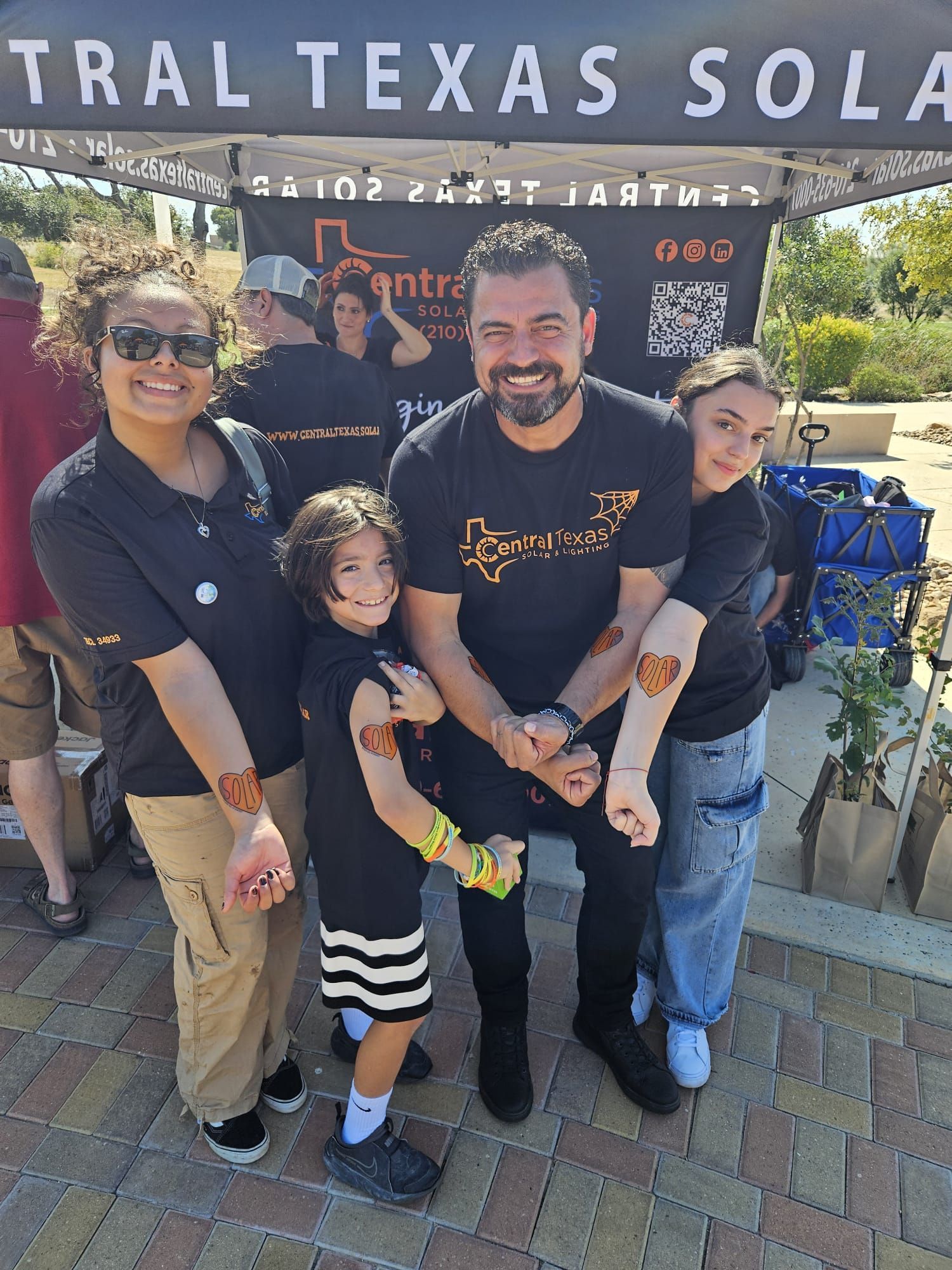 Family posing at a festival booth under a Texas Solar canopy, smiling and holding a child.