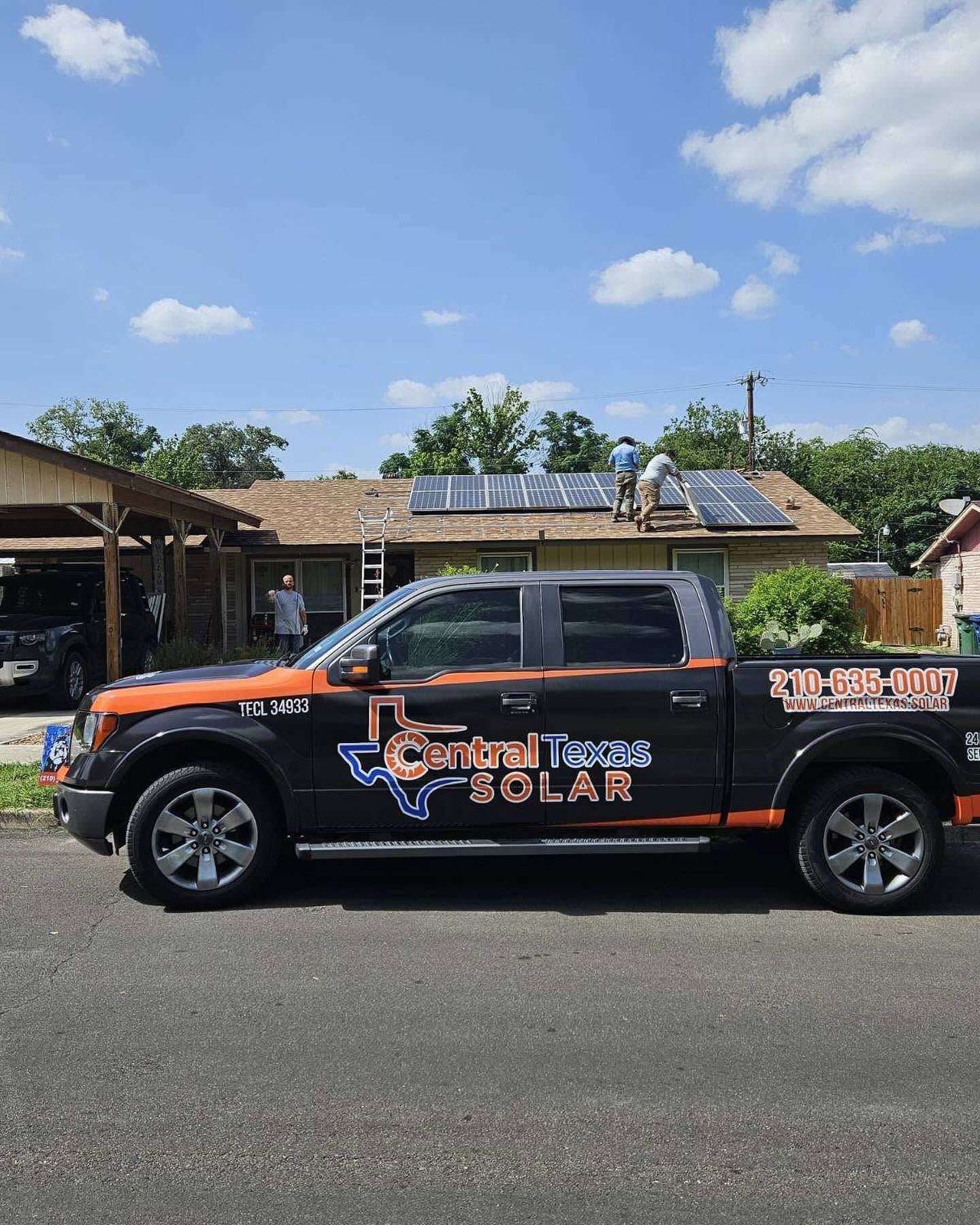 Black pickup truck with “Solar” company branding parked on a street under a blue sky.