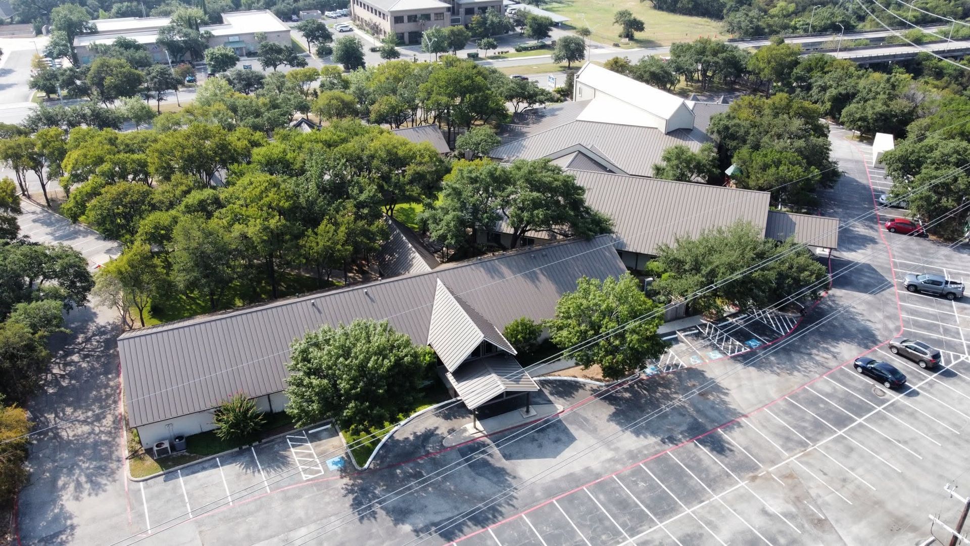 Aerial view of a building with a parking lot, trees, and surrounding streets