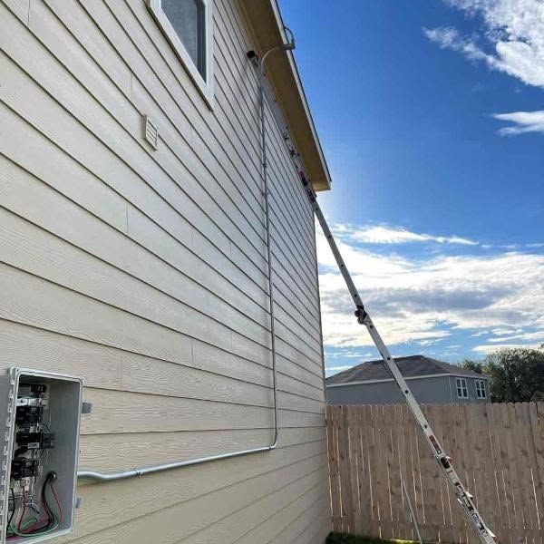 Side of a white house with an electrical panel open and a ladder leaning against the wall under a blue sky