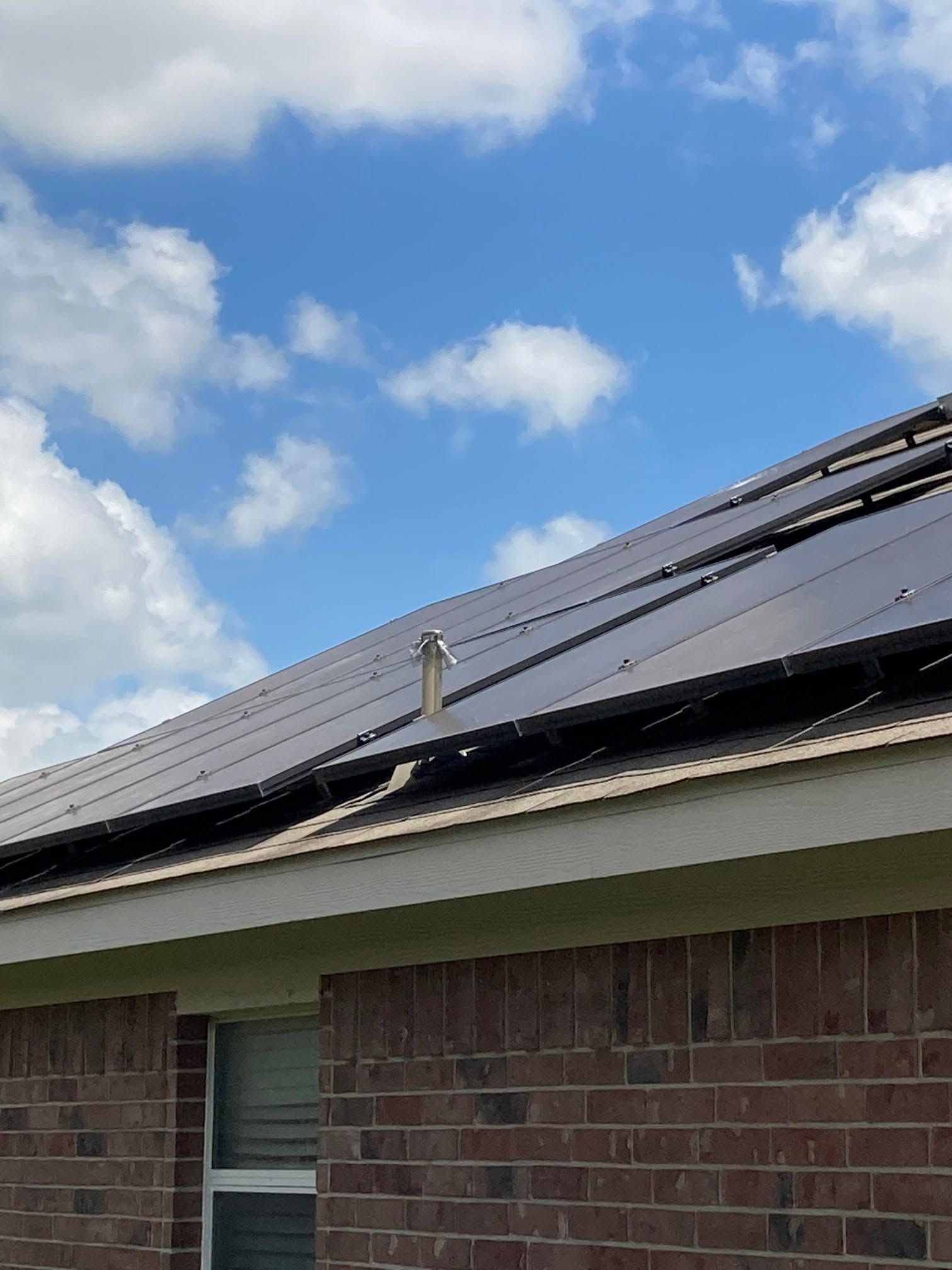 Solar panels mounted on a sloped roof above a brick house under a partly cloudy sky