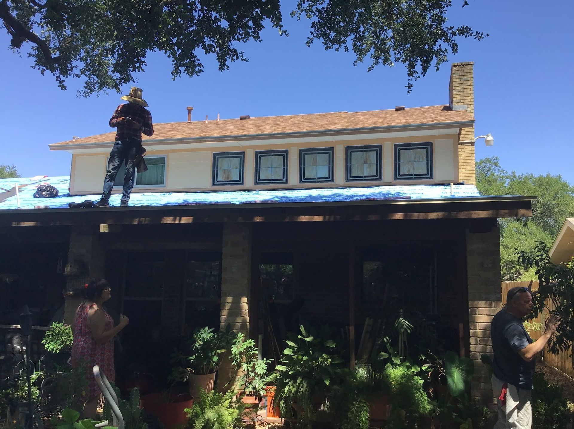 Worker on a roof above a house with a porch and trees in the foreground