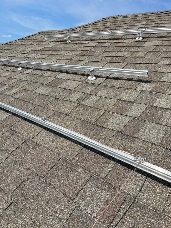 Roof shingles with several metal mounting rails and brackets for solar panels under a blue sky