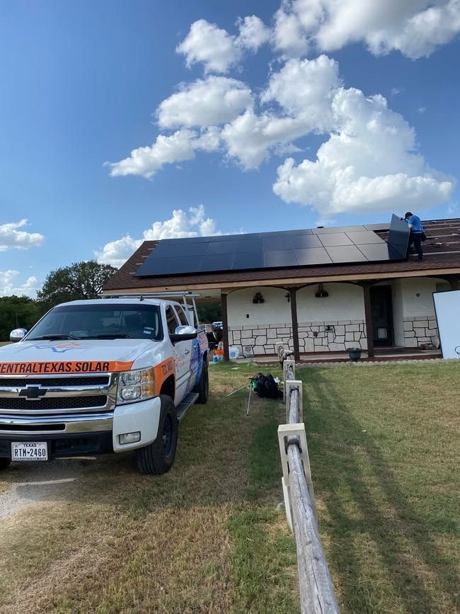 Pickup truck parked by a house with solar panels under a cloudy blue sky