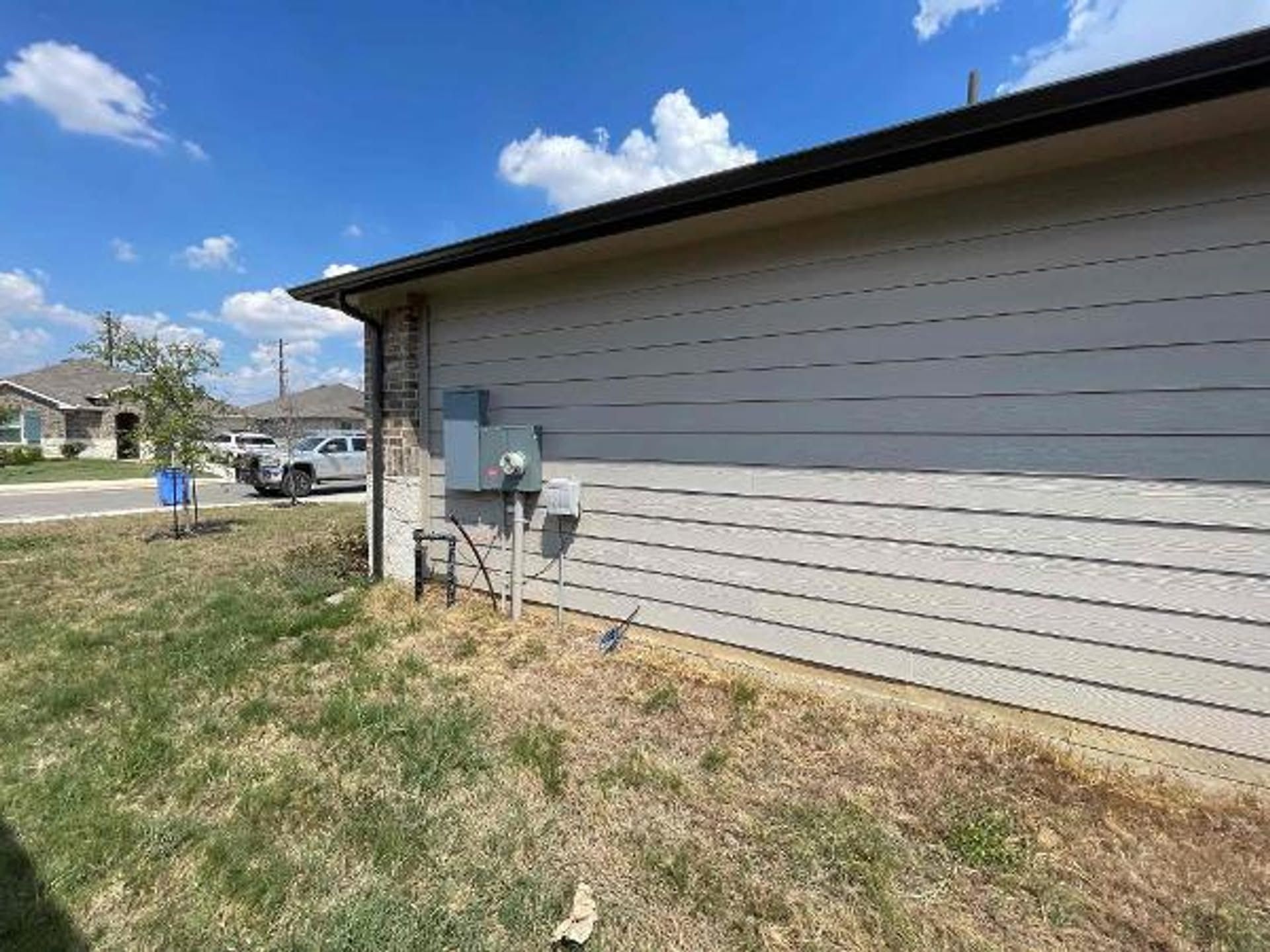 Side of a beige house with a utility meter, grass yard, and blue sky with clouds.