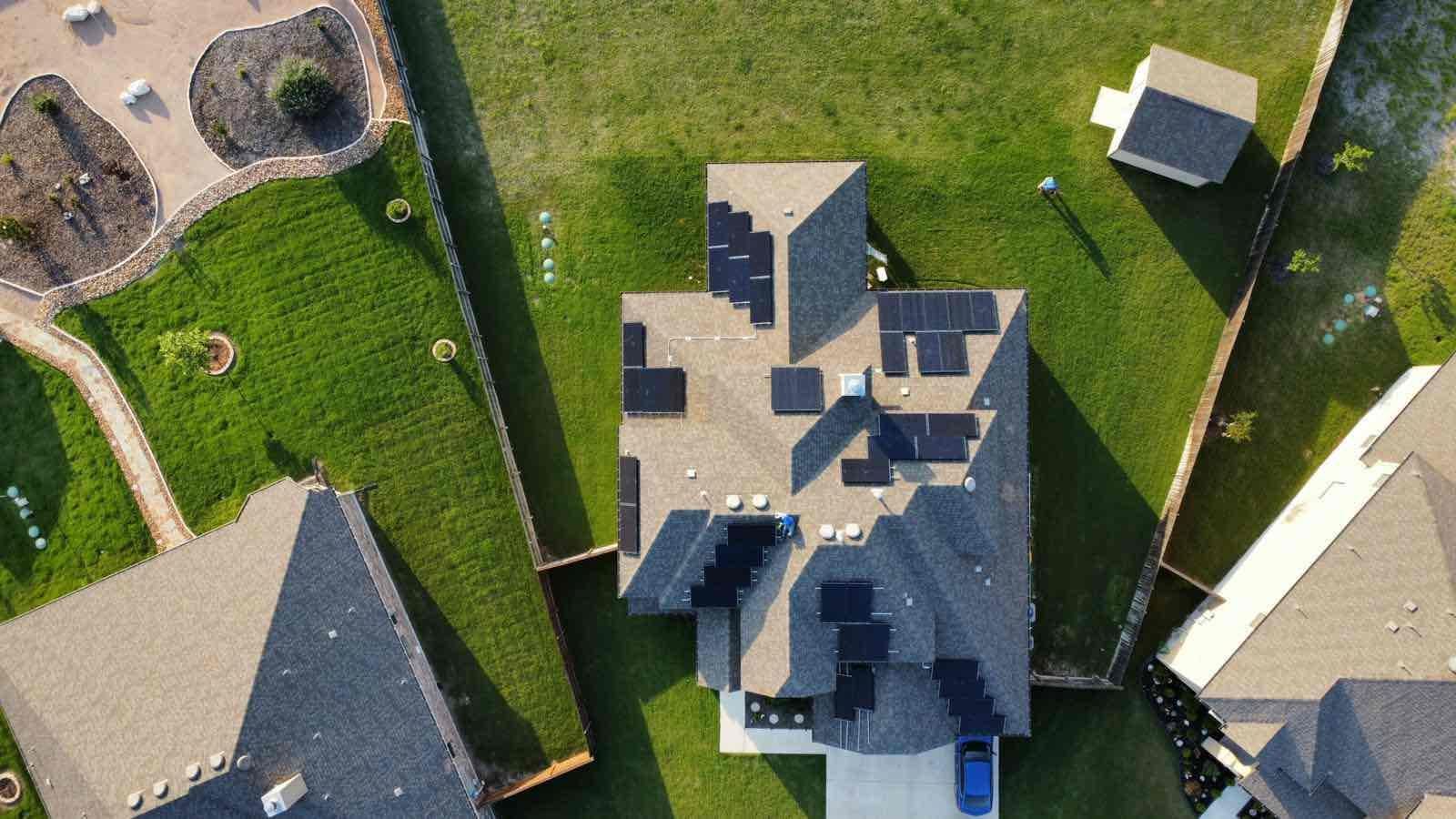 Aerial view of a gray-roofed house with green lawn and neighboring homes.