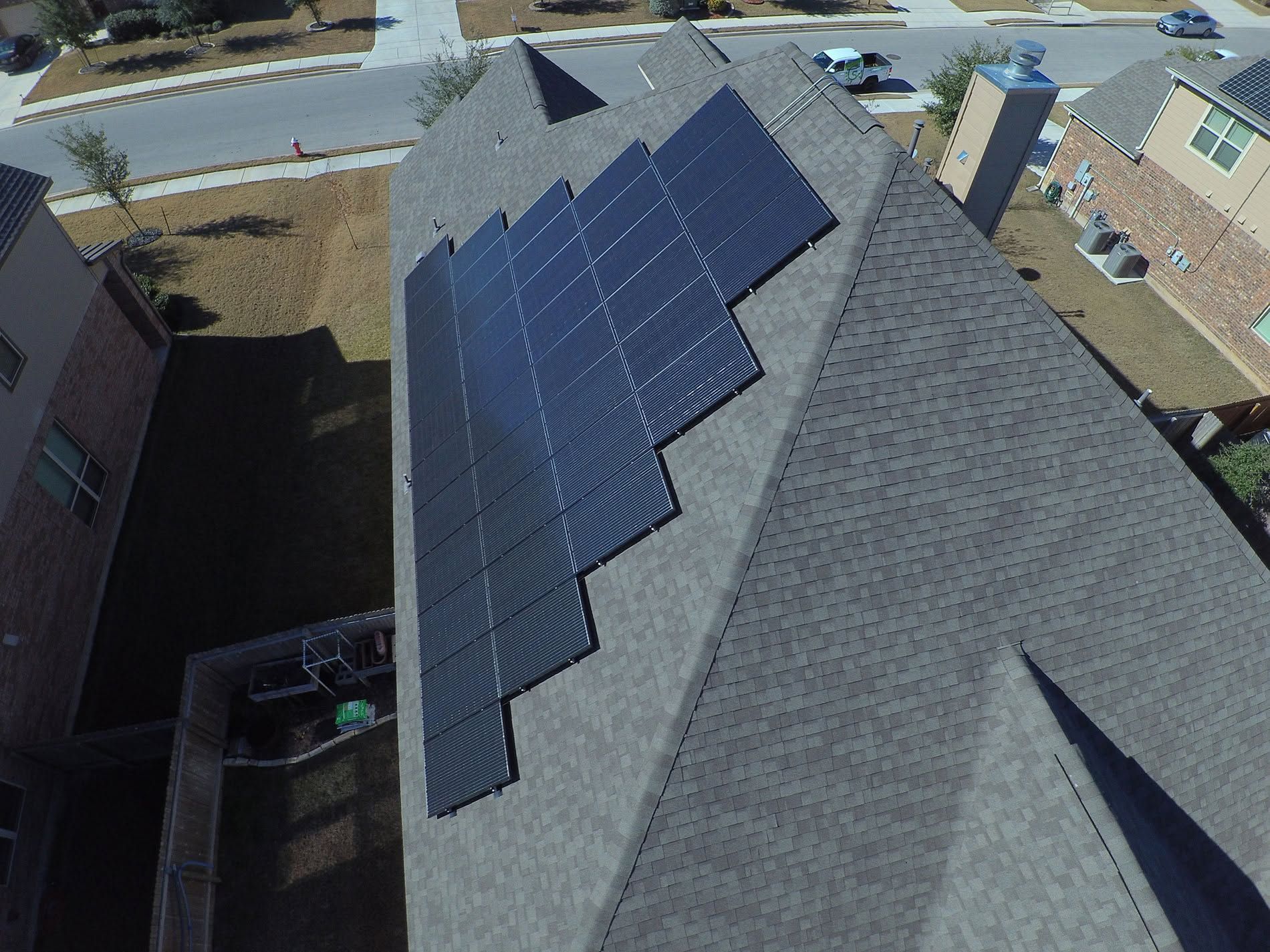 Rooftop with rows of dark solar panels on gray shingles in a residential neighborhood