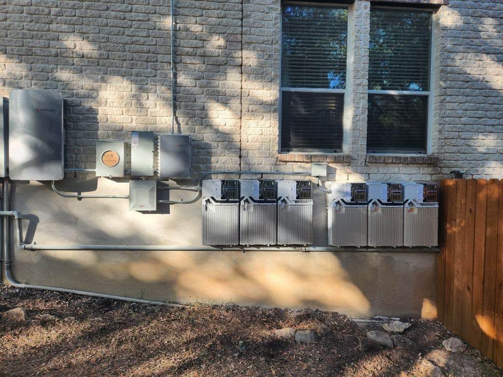 Row of electrical meter boxes and utility panels on a brick house exterior beside a window and wooden fence