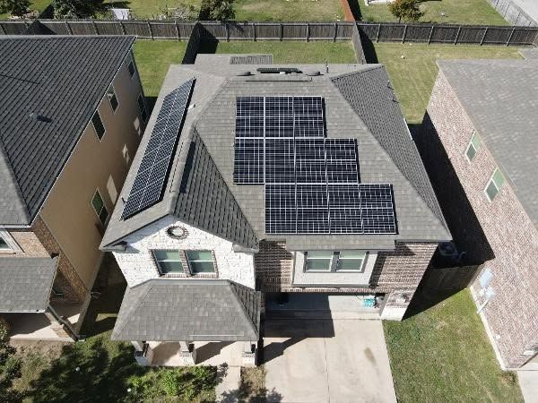 Aerial view of a house with dark roof tiles and solar panels in a suburban neighborhood
