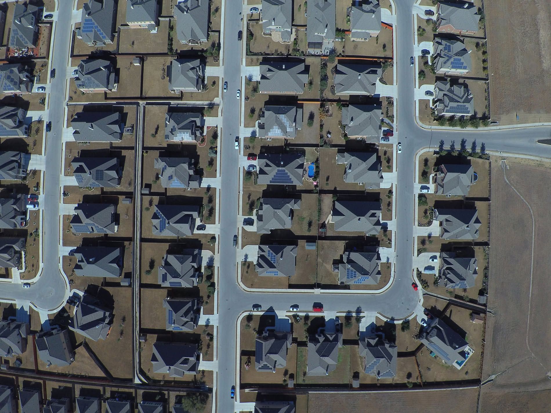Aerial view of a suburban neighborhood with rows of houses, streets, and open fields.