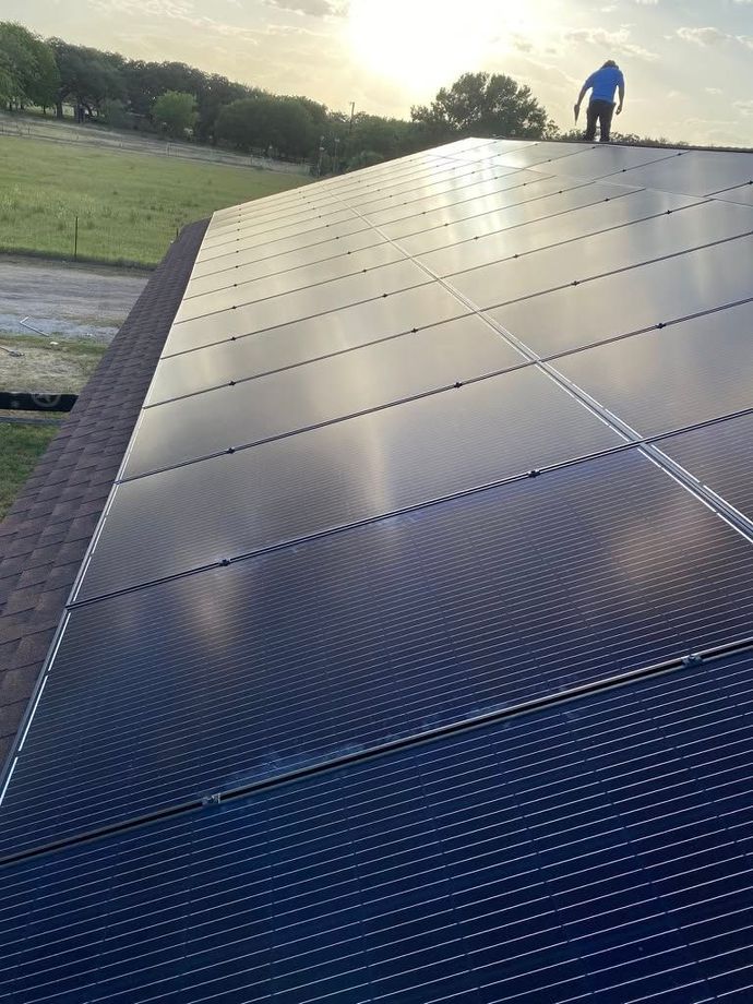 Solar panels on a sloped roof at sunset, with a person standing near the top edge.